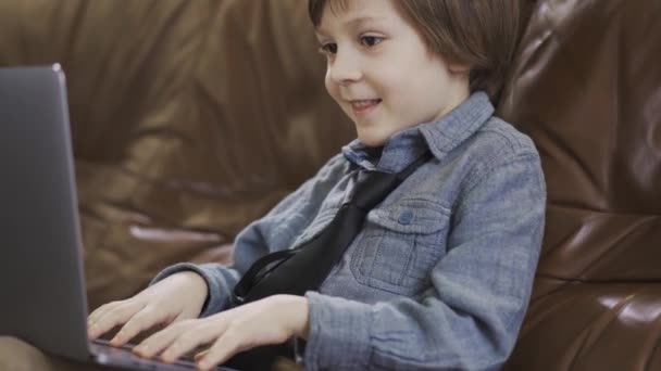 Niño Con Chaqueta Vaquera Sentado Sofá Cuero Jugando Portátil Sonriendo — Vídeos de Stock