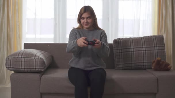 胖女孩坐在家里的沙发上玩电子游戏 胖女人手里拿着操纵杆 女士在家 — 图库视频影像