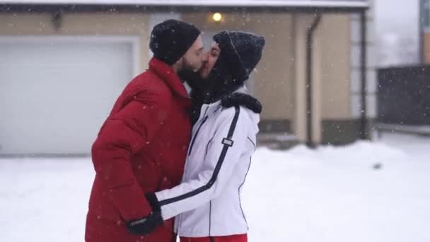 髭を生やした男ときれいな女性が冬の裏庭でキスをする 男は手袋で指で女の子の唇に触れよう 両方の人が笑って ビデオ — ストック動画