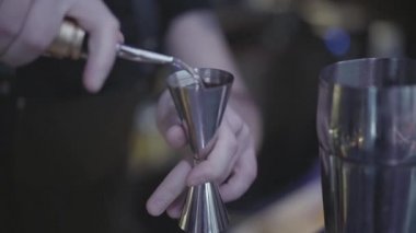 Barmen elinin ölçü kabından bardağa su doldurduğu yakın çekim. Kokteyl hazırlama.