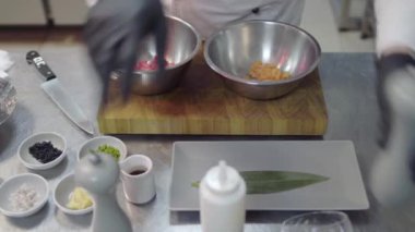 Kesme tahtasına iki metal kase, dilimlenmiş somon balığı ve ton balığı. Lokanta mutfağında yemek hazırlayan siyah lateks eldivenli eller..