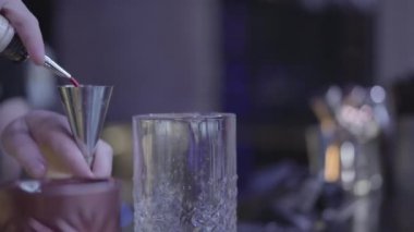 Barmen elinin ölçü kabından bardağa su doldurduğu yakın çekim. Kokteyl hazırlama.