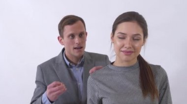 Portrait of genuine man in gray suit puts a pendant on the neck of a girl close up. Woman is happy because of a gift. Emotional young woman receive present from her boyfriend. Shooting in the studio on a white background