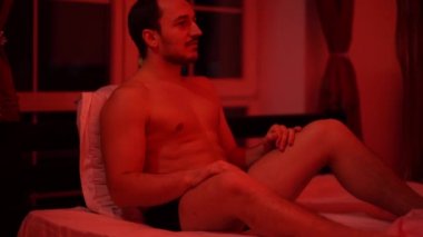 Genç adam samimi bir ortamda yatakta oturur, çarpıcı bir vücudu olan bir kız yanına gelir ve bacaklarını ayırır, heyecanlanır.