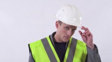 Yakışıklı, kendine güvenen, beyaz arka planda duran beyaz şapkasını tamir eden genç bir adam..