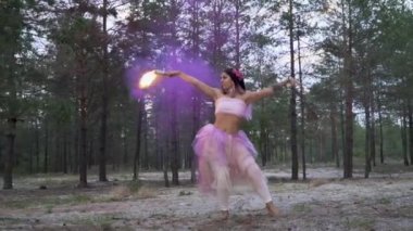 Pembe elbiseli, parlak makyajlı güzel bir kız. Arka planda yanan sis bombalarıyla dans ediyor..