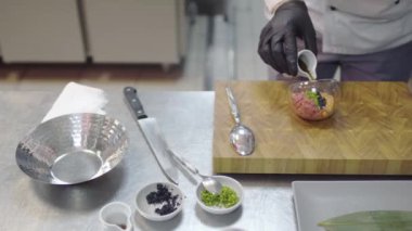 Modern restoran mutfağında siyah lastik eldivenli şef ton balığı ve somon balığı hazırlıyor. Erkek, yemeğe baharat katıyor. Lezzetli yemek hazırlama konsepti. Üst görünüm