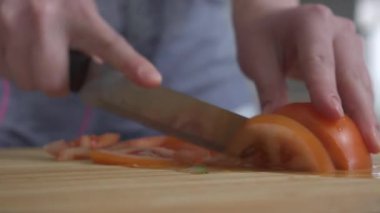 Kadın eli, mutfak tahtasında bıçakla domatesleri ince dilimlere ayırıyor. 