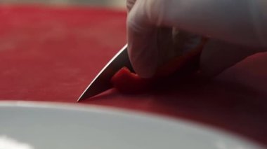 Eller beyaz kauçuk şefin eldivenleriyle pişirir. Bıçakla yakın plan bir biber dilimini keser..