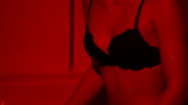 Siyah sutyenli genç kadının göğüsleri kırmızı ışıkta birbirine yaklaşıyor. Kızın derisi ıslanmış. Tutkulu kadın sakin duruyor, saçları uçuşuyor.