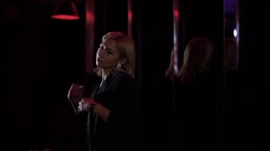 Gece kulübünde dans eden parlak küpeli yetişkin sarışın kadın. Bayan eğleniyor, vücudunu diskoya götürüyor. Partiye katılanların boş vakitleri