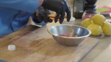 Siyah lastik eldivenli usta aşçının elleri restoranın mutfağında doğranmış etle alüminyum kasedeki şişeden yağ döküyor. Yemek hazırlama.