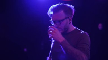 Diskoda elinde bir bardak alkolle dikilen rahat bir adamın portresi. Gözlüklü yetişkin adam kameraya bakıyor ve kokteylini içiyor. Partiye katılanların boş vakitleri