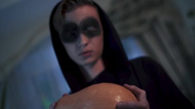 Korkunç makyajlı bir adam elinde balkabağı tutan siyah elbiseli bir adam. Cadılar Bayramı tatili, video 