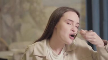 Uzun siyah saçlı güzel bir kadın restoran masasında oturup lezzetli yemekler yiyor.