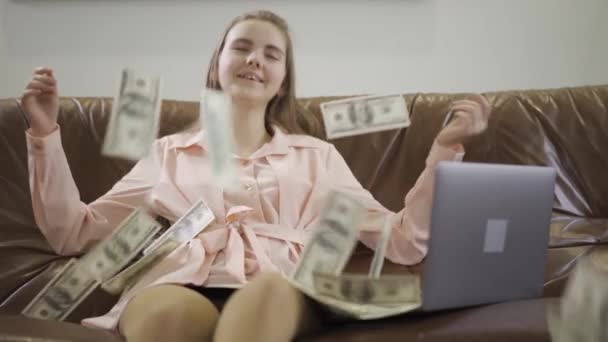 ラップトップの前の革のソファに座っているかなり十代の女の子 ドルは女の子に落ち 子供は笑顔と満足しています 金持ちの親の子 スローモーション — ストック動画