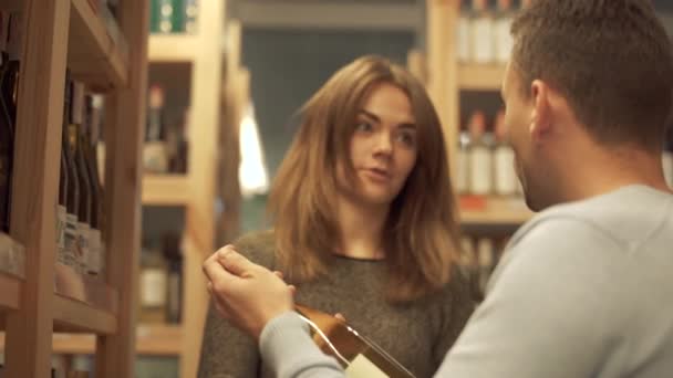 ハンサムな男がワインを持っている アルコールショップでドリンクを選ぶお客様 男性と女性はアルコールについて議論しています — ストック動画
