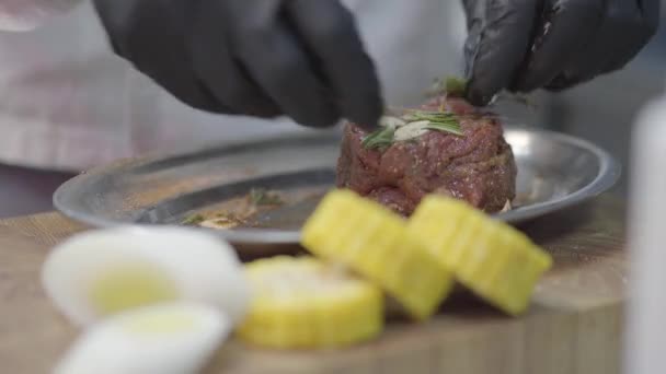 厨师们手戴黑色手套 在金属板上揉搓一块小牛肉 将肉腌化 靠近盘子的甜玉米 — 图库视频影像
