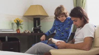 Koltuğunda oturan iki kardeş, yakışıklı ağabey sevimli küçük kardeşe bir kitap okudu ve çok güldüler..