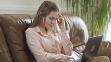 Konsantre olmuş zarif kız deri koltukta oturmuş dizüstü bilgisayarın klavyesine yazı yazıyor. Modern gençlerin boş vakitleri. Aletlere bağımlılık. Sağlık konsepti, zengin hayat.