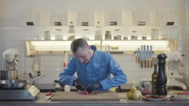 Restoran üniformalı sarışın aşçı ve siyah eldivenli adam modern mutfakta duruyor. Etrafta bir sürü mutfak gereçleri var ve ton balığı dilimleri kesiyorlar..