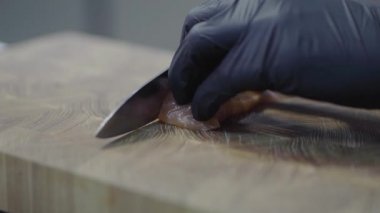 Modern restoranın ahşap tahtasında somon kesen siyah lastik eldivenli şefin elleri. Deniz ürünleri hazırlığı. Şef suşi yapıyor. Yavaş çekim