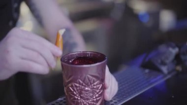 Tanınmayan genç barmen, ziyaretçiye servis etmeden önce portakal kabuğuyla kilden bir bardak kokteyl ovuyor. Gece hayatı, gece eğlencesi. Barmen alkol içiriyor.