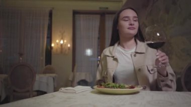 Güzel servis edilen erişteleri roka ile yiyen genç bir kadın kırmızı şarap içip birine gülümsüyor.