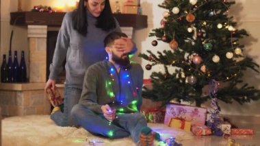 Genç, pozitif bir çift, Noel ağacında, odada, yerde oturuyor. Kadın adama hediye kutusu veriyor, video. 