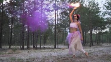 Pembe elbiseli, parlak makyajlı güzel bir kız. Arka planda yanan sis bombalarıyla dans ediyor..