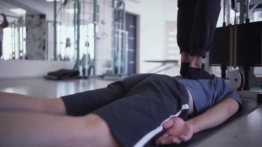 Erkeklerin bacakları, spor salonunda erkeklerin sırtına basıyor. Bir adam diğerinin üzerine basarak masaj yapıyor. Gençlerin sağlıklı yaşam tarzı