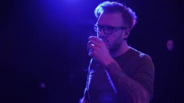 Elinde dövmesi olan bir adam gece kulübünde viski içiyor. Yalnız adam müziğin ritminde dans ediyor. Parlayan ışıkta duruyor.