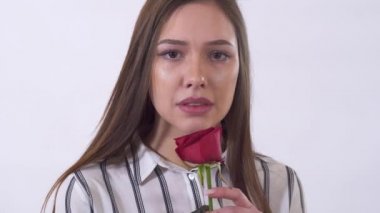 Portrait of sad young woman, crying close up. Lady holding rose in hands. Woman is depressed, disappointed her face shows grief. Shooting in the studio on a white background