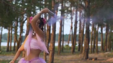 Pembe elbiseli, parlak makyajlı güzel bir kız. Arka planda sis bombalarıyla dans ediyor..