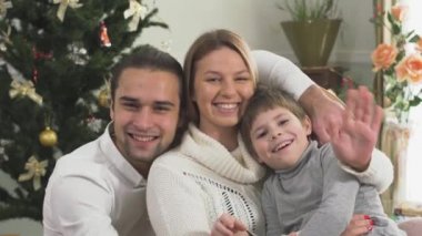 Evde Noel ağacının yanında oturan baba, anne ve oğulun mutlu aile portresi. Karı ve koca birlikte mutlular. İnsanlar birbirine sarılır ve el sallar.