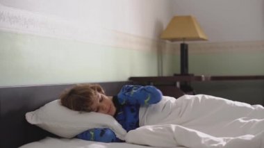 Pijamalı, dağınık saçlı küçük bir çocuğun portresi. Sabah kalkar ve yatak odasından çıkar.