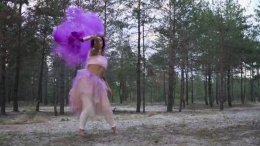 Pembe elbiseli, parlak makyajlı güzel bir kız. Arka planda yanan sis bombalarıyla dans ediyor..