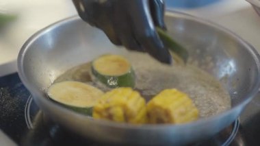 Siyah lateks eldivenleri teslim et. Sıcak tavaya kabak ve mısır koy. Kızarmış sebze.