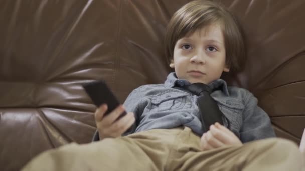 Uroczy Chłopiec Siedzący Skórzanej Kanapie Rozłożonymi Nogami Zmieniający Kanały Pomocą — Wideo stockowe