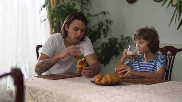 Dwóch Przystojnych Braci Siedzących Przy Kuchennym Stole Jedzących Rogaliki Cappuccino — Wideo stockowe
