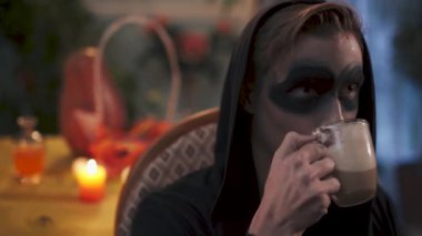 Siyah içecekler içindeki genç sihirbaz kakao içiyor. Cadılar Bayramı tatili, video 
