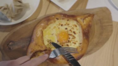 Erkek eller çatala bıçağı sürterek yiyeceğe hazırlanıyor. Ajarian khachapuri Gürcistan peynirli turtası. Kafedeki tahta tahtada servis ediliyor..