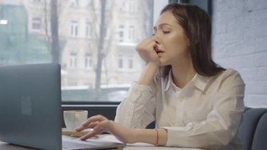 Kafedeki masada oturan mutsuz kadın dizüstü bilgisayarını kullanıyor. Pencerenin yanındaki kanepede oturan kız bilgisayarla çalışıyor. Üzgün kadın çalışmanın sonucundan memnun değil.