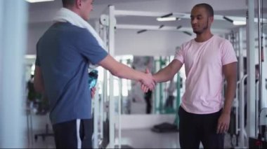 Afrikalı Amerikalı bir adam spor salonunda beyaz bir adamla tokalaşıyor. Spor salonunda iki genç adam. Koç ve koğuş.