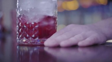 Bir bardak buz, içinde kırmızı içecek, barın üstünde el. Bardakta sıvı karışımı. Parti zamanı.