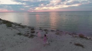 Pembe elbiseli, parlak makyajlı, nehrin kıyısında sis bombalarıyla dans eden tatlı bir genç kadın. Çiçekli, harika bir saç stili olan güzel, şehvetli bir kızın dansı. Yavaş çekim.