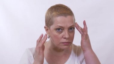 Olgun, mutsuz bir kadının kameraya bakıp kırışıklıkları olan yüzü için endişelendiği bir video.