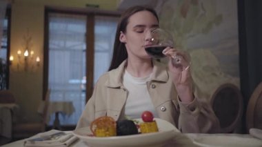 Genç bir kadın güzel bir şekilde iştah açıcı biftek ya da kuzu eti, ızgara mısır, kabak ve bir bardak kırmızı şarap ile doğruyor ve yiyor.