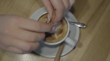 Kafedeki bir masada kapuçino fincanı. Yakın plan. Kızın eli kahveye şeker koyar, bir kaşık alır ve onu yakınlaştırır. Üst görünüm