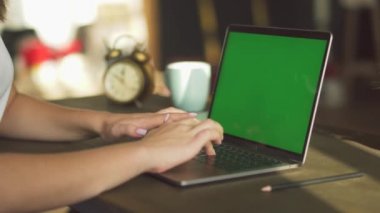 Yeşil ekranlı bir dizüstü bilgisayarda çalışan bir kadının yakın çekim görüntüsü.